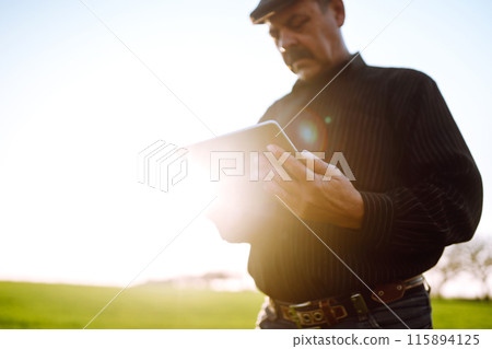 Farmer owner using touchpad for check wheat field at sunset. Farmer working with digital tablet. Farmer owner using touchpad for check wheat field at sunset. Farmer working with digital tablet. 115894125