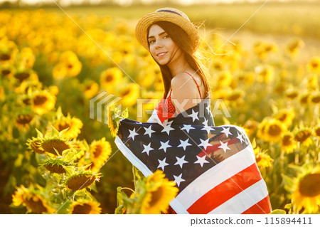 Beautiful girl in hat with the American flag in a sunflower field. 4th of July. Fourth of July. Freedom 115894411