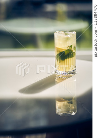A glass of iced lemonade with slices of fresh lemon and mint leaves on a refreshing light background. Cool the freshly made lemonade, with space to copy. High quality photo 115894470