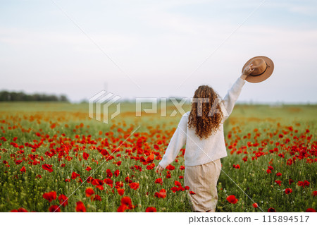 Back view. Young curly woman in hat posing in the poppy field. Summer landscape. 115894517
