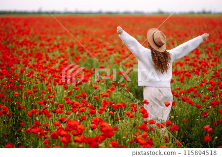 Back view. Young curly woman in hat posing in the poppy field. Summer landscape. Back view. Young curly woman in hat posing in the poppy field. Summer landscape. 115894518