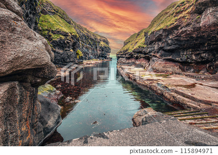 Calm water reflecting dramatic sky in gjogv, faroe islands 115894971