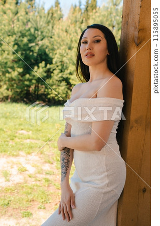 Woman In White Dress Leans Against Wooden Post During Summer Day 115895055