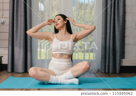 Woman in White Sports Bra and Shorts Sitting in a Yoga Pose in Front of a Window 115895062