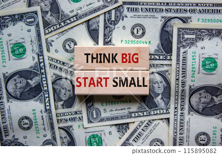 Think big start small symbol. Concept words 'Think big start small' on wooden blocks on a beautiful background from dollar bills. Business, motivational and think big start small concept. Think big start small symbol. Concept words 'Think big start small' on wooden blocks on a beautiful background from dollar bills. Business, motivational and think big start small concept. 115895082