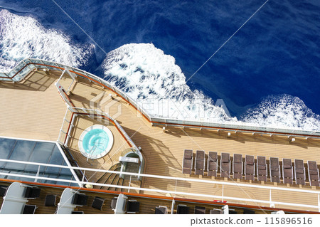 A fragment of the plank deck of a luxury cruise ship with brown sun loungers and a round jacuzzi 115896516