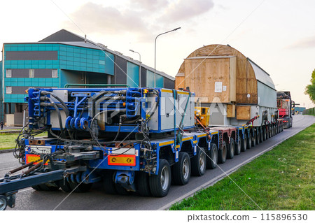 Very long specialized multi axle truck trailer carries very heavy oversize load, rear view 115896530