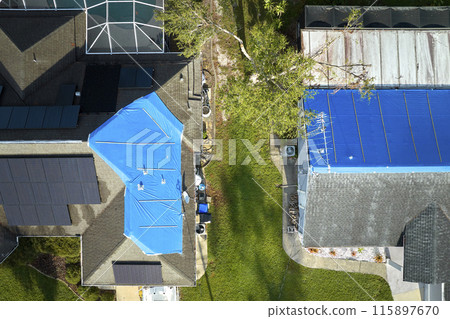 Aerial view of damaged in hurricane Ian houses roofs covered with blue protective tarp against rain water leaking until replacement of asphalt shingles 115897670