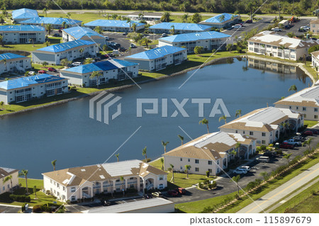 Aerial view of damaged in hurricane apartment building roofs covered with blue protective tarp against rain water leaking until replacement of asphalt shingles 115897679