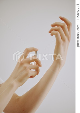 Female hands holding small flask with transparent aroma and spraying it on her wrist 115897721