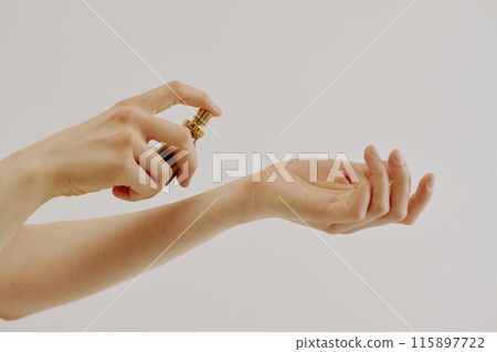 Female manicured hands holding brown glass flask full of new aroma and spraying it on her wrist Female manicured hands holding brown glass flask full of new aroma and spraying it on her wrist 115897722