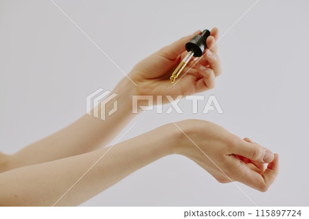Womans manicured hand holding glass pipette full of golden aromatic essence and dripping it Womans manicured hand holding glass pipette full of golden aromatic essence and dripping it 115897724