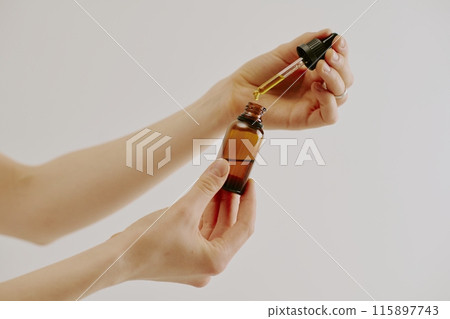 Female hands holding brown glass bottle and glass pipette full of organic golden essence 115897743