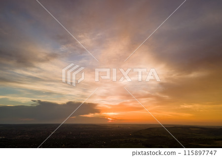 Bright colorful sunset sky with setting sun and vibrant clouds over dark landscape Bright colorful sunset sky with setting sun and vibrant clouds over dark landscape 115897747