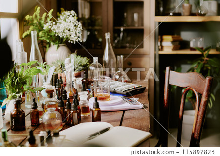 Old wooden table with huge number of small brown glass bottles with essential oils perfume sample, green houseplant in white clay pots and white round clay vase with bouquet 115897823