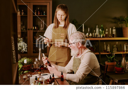 Senior male perfumer showing new perfume samples while his young female assistant standing near him and making notes 115897866