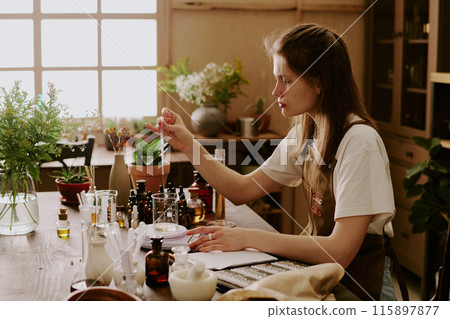 Young perfumer weighing glass flask with organic essence and adding new essential oil 115897877