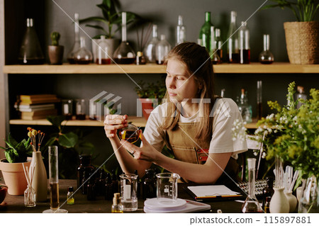 Young female perfumer admiring new samples of handmade perfume in home lab Young female perfumer admiring new samples of handmade perfume in home lab 115897881