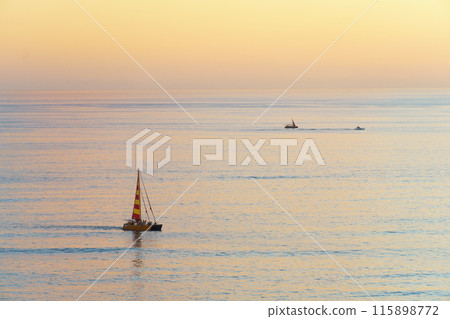 A sailboat glides on calm water under an open sky A sailboat glides on calm water under an open sky 115898772