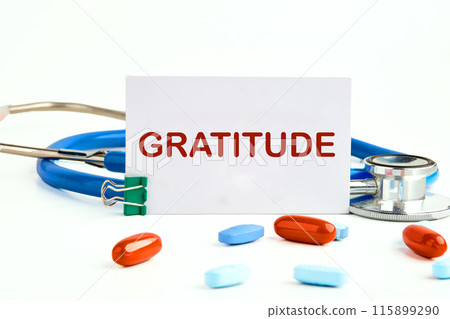 GRATITUDE Writing on a business card next to a stethoscope with pills, vitamins GRATITUDE Writing on a business card next to a stethoscope with pills, vitamins 115899290