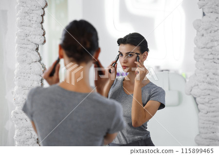 A young woman massages her face with gouache while looking in the mirror. A young woman massages her face with gouache while looking in the mirror. 115899465