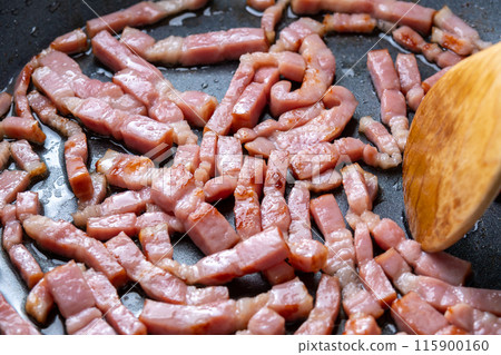 A cooking scene in which bacon cut into strips is fried in a frying pan. A cooking scene in which bacon cut into strips is fried in a frying pan. 115900160