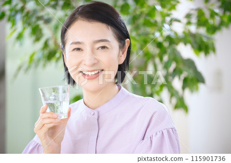 Smiling middle-aged woman drinking water in the living room Smiling middle-aged woman drinking water in the living room 115901736