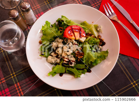 Plate with salad with lettuce, nuts, tomato and brie cheese on table 115902666