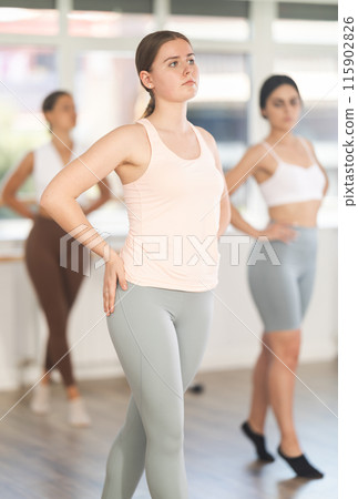 Warm-up sessions. Cheerful fit active young girl training various ballet poses during group classes with ballet dancers, rehearsal before performance in choreography studio Warm-up sessions. Cheerful fit active young girl training various ballet poses during group classes with ballet dancers, rehearsal before performance in choreography studio 115902826