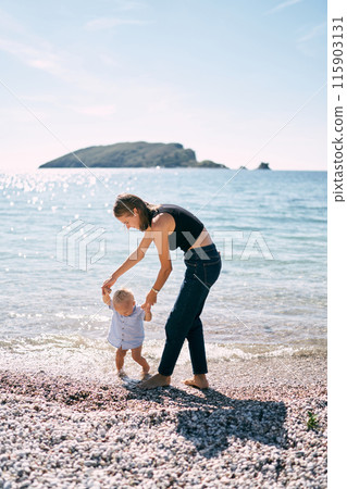 Mom leads a little boy by the hands along the seashore. High quality photo 115903131