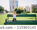 Little girl sits on a bench on her knees and leans on the back with her hands. High quality photo 115903145