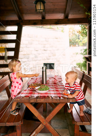 Little girl at the table offers a salad to a little boy. High quality photo 115903154