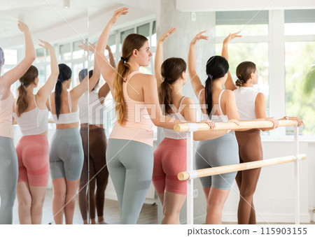 Group ballet rehearsal - young ballerinas stand in third position near ballet barre during group training in dance studio Group ballet rehearsal - young ballerinas stand in third position near ballet barre during group training in dance studio 115903155