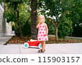 Little girl stands near a toy car on a paved path in the garden. High quality photo 115903157