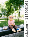 Little girl in sunglasses sits on a bench next to a lunch box. High quality photo 115903161