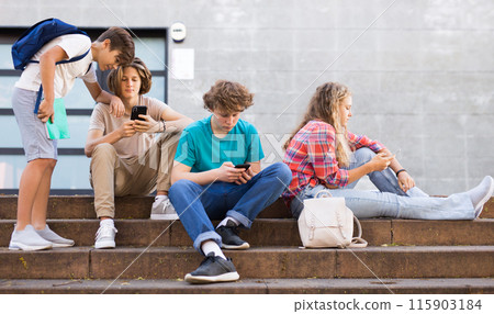 Teenager girl and boys sitting front college with smartphones 115903184