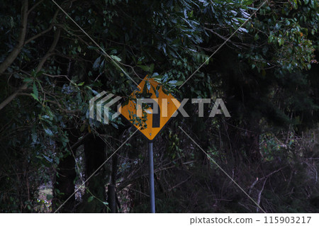 Yellow road sign with curved black arrow covered in leaves 115903217