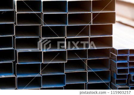 Industrial warehouse stock of rectangular metal pipes for building and construction supplies. Stack of steel pipes. Iron materials for construction and infrastructure projects. Steel tubing storage. 115903257