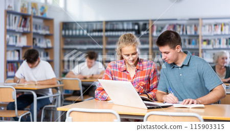 European schoolgirl with a classmate in the library is preparing for lessons 115903315