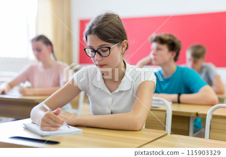 High school student teenage girl studying in college with classmates, making notes of teacher lecture High school student teenage girl studying in college with classmates, making notes of teacher lecture 115903329