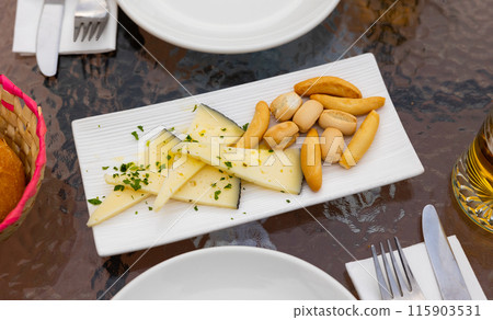 On wooden table there is serving board with sliced cheese manchego and crotone On wooden table there is serving board with sliced cheese manchego and crotone 115903531