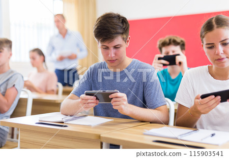 Young students with smartphones sitting in class room 115903541