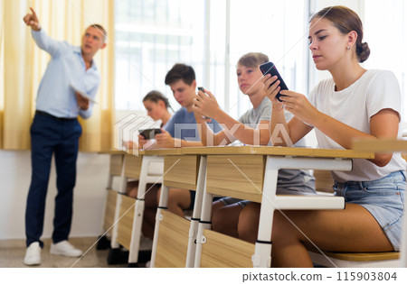 Girl high school student using mobile phone on lecture in class Girl high school student using mobile phone on lecture in class 115903804