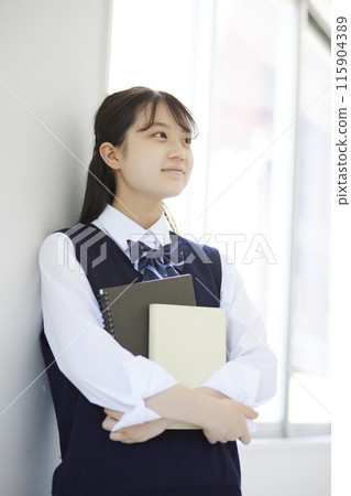 A high school girl leaning against a wall with a textbook 115904389