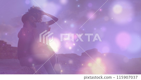 Image of glowing spots of light over african american couple sitting on the rocks near the sea Image of glowing spots of light over african american couple sitting on the rocks near the sea 115907037