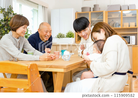 祖父和祖母一家人圍坐在客廳的桌子旁，享受著兒子和妻子的孩子。 115909582