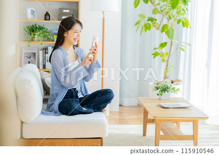 Young woman relaxing in the living room and looking at her smartphone Young woman relaxing in the living room and looking at her smartphone 115910546
