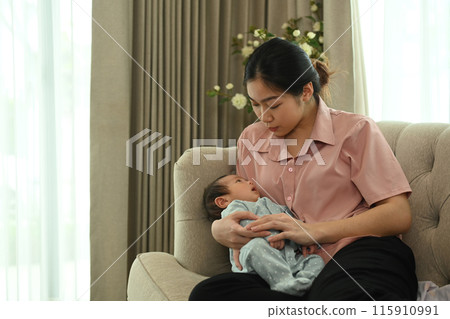 Asian young mother sitting on a sofa and holding a newborn baby in her arms. Motherhood concept 115910991