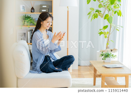 Young woman relaxing in the living room and looking at her smartphone Young woman relaxing in the living room and looking at her smartphone 115911440