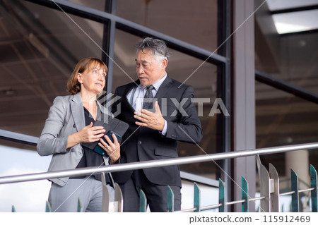 Two senior business man and woman in formal meeting and discussing documents and using a tablet. 115912469